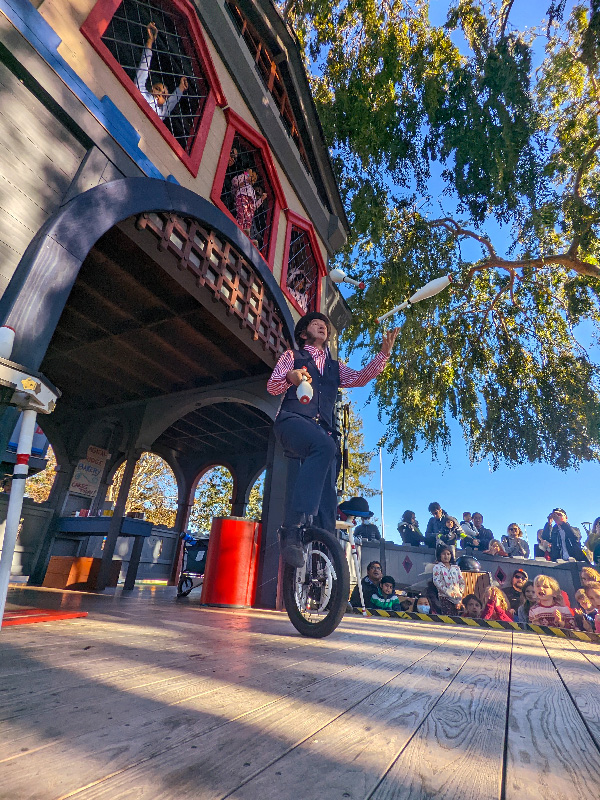 Slim juggling pins on a unicycle in front of young audience