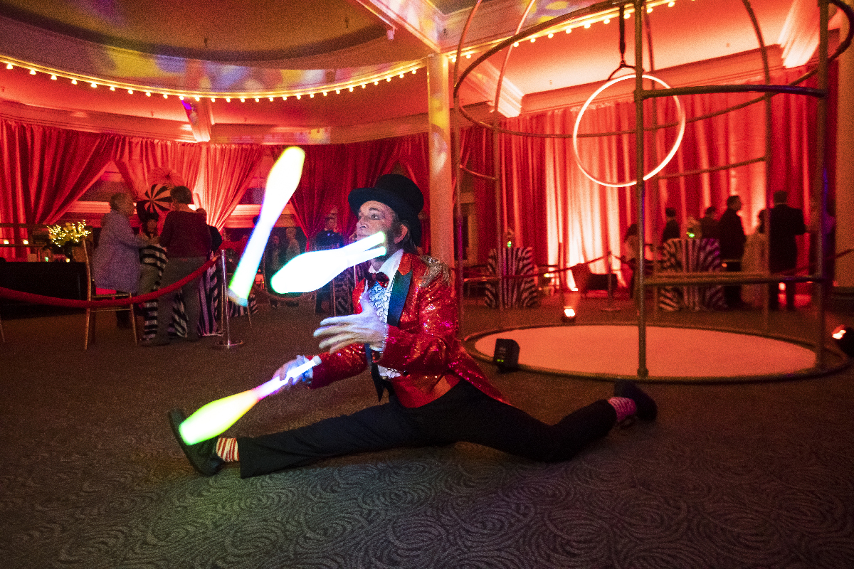 Slim juggling LED pins in a red lit performance space with an aerial hoop