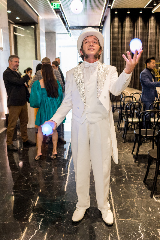 Slim juggling LED balls in a white suit and top hat at an indoor event