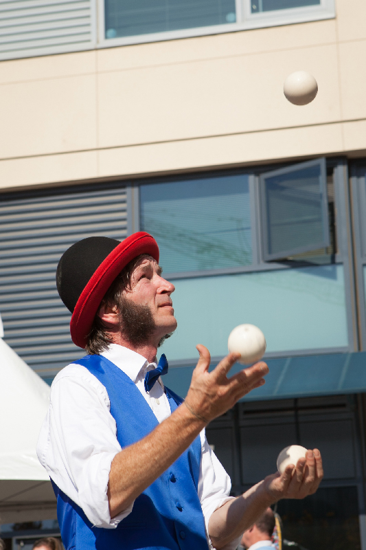 Slim juggling balls on a street in a blue vest, bowtie, and red and black bowler hat